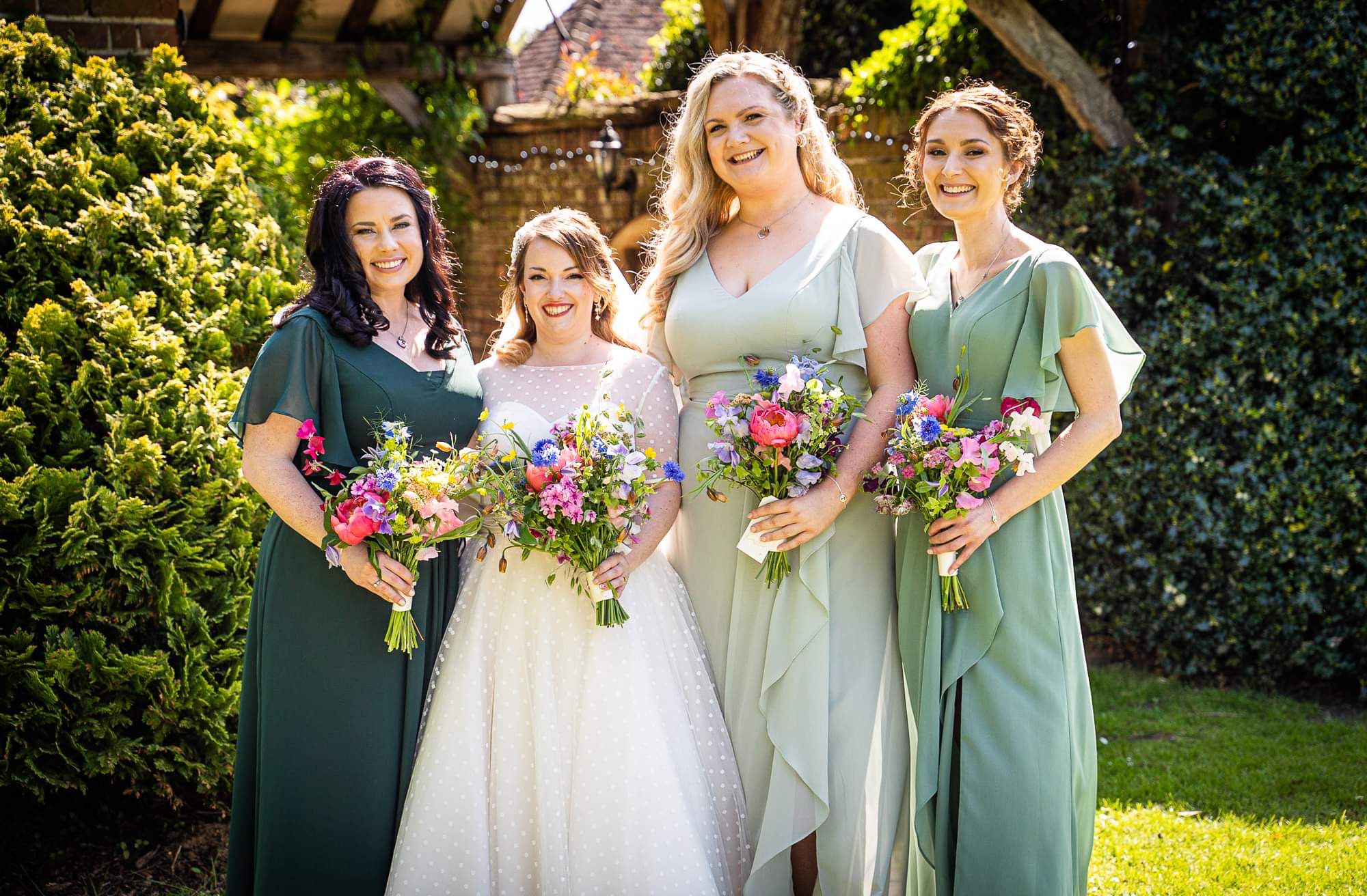 Bride and three bridesmaids posing together outdoors with floral bouquets.